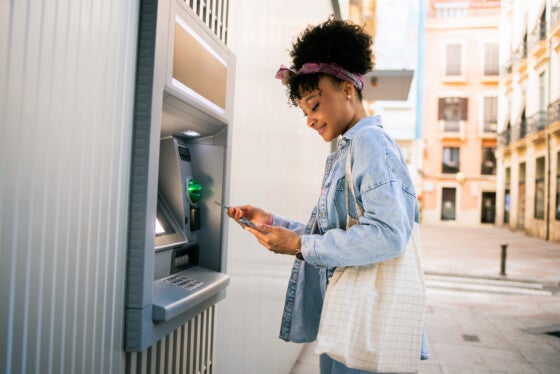 Young multiracial woman taking the money from the ATM machine for shopping.