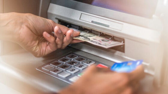 Close up of hand holding dollar banknotes from ATM machine and credit card in the other hand.