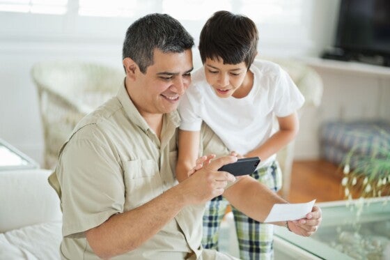 Father and son depositing bank slip together through smart phone in living room