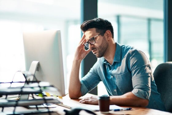 Shot of a young businessman looking displeased while using a computer at his work desk