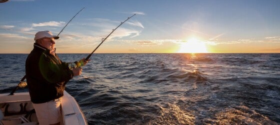 Man fishing on the ocean from the back of his boat at sunset