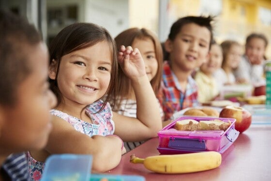 Elementary school kids sitting a table with packed lunches