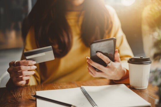 Young woman using smart phone and credit card for shopping online in coffee shop cafe, vintage tone color