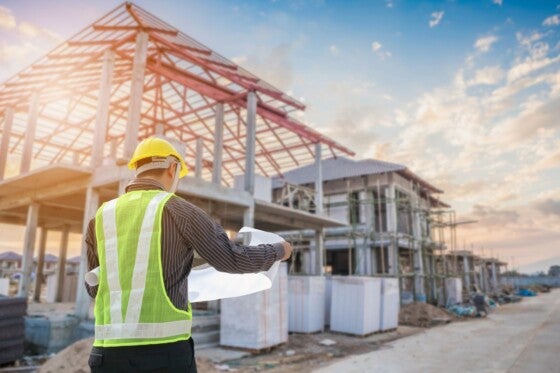 Professional engineer architect worker with protective helmet and blueprints paper at house building construction site background