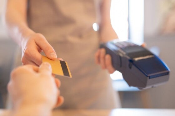 Young waitress in apron giving back credit card of businessman after payment for lunch through electronic machine