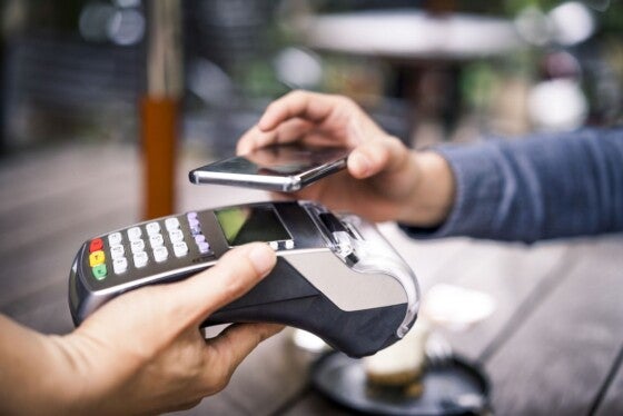 Close-up of customer paying for his coffee through mobile payment. Owner is holding credit card reader. They are in cafe.