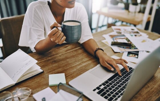 Cropped shot of a businesswoman using a laptop and having coffee while working in her home office