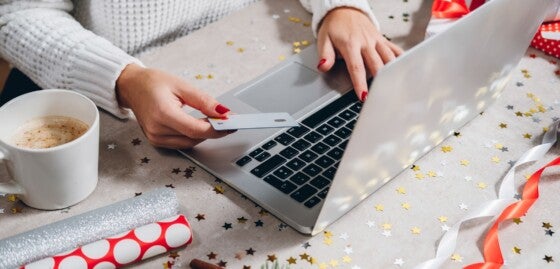 Christmas online shopping top view. Woman buying presents online with silver credit card and laptop computer, drinks coffee among gift boxes. Winter holidays sales concept