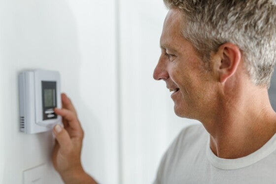 A Smiling Man Adjusting Thermostat On Home Heating System