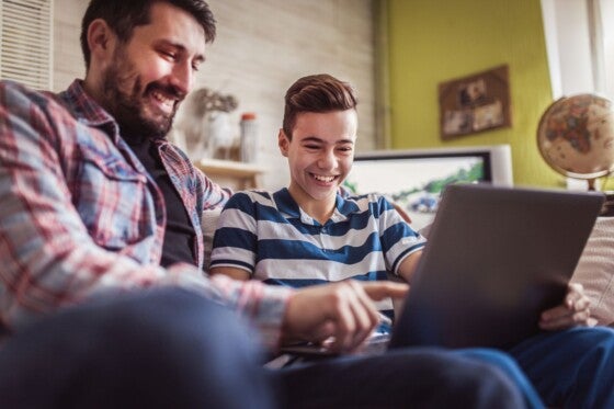 Smiling father and son using digital gadgets in living room