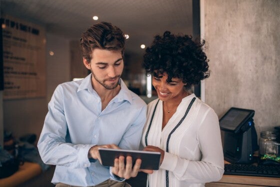 Two restaurant business partners standing together and looking at digital tablet. Man and woman using digital tablet in a cafe.