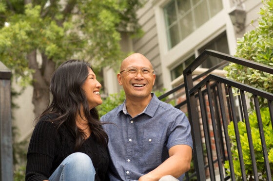 Portrait of an Asian couple smiling and hugging outside.