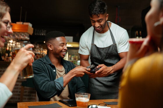 diverse friends out for dinner at restaurant paying with cellular device