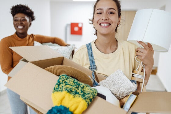 Two female friends carrying cardboard boxes with belongings and moving into campus