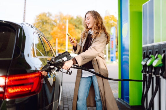 Woman filling up car at gas station while consulting phone