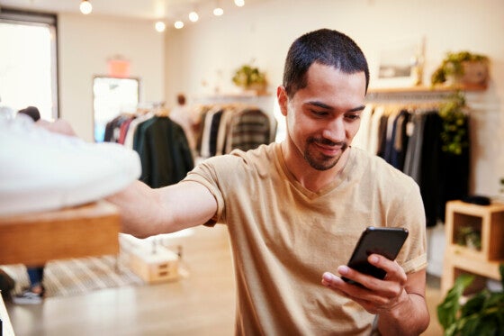 Smiling Hispanic man using smartphone in a clothes shop